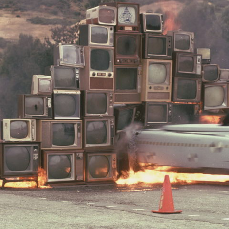 An airplane on a runway crashing through a collection of television screens